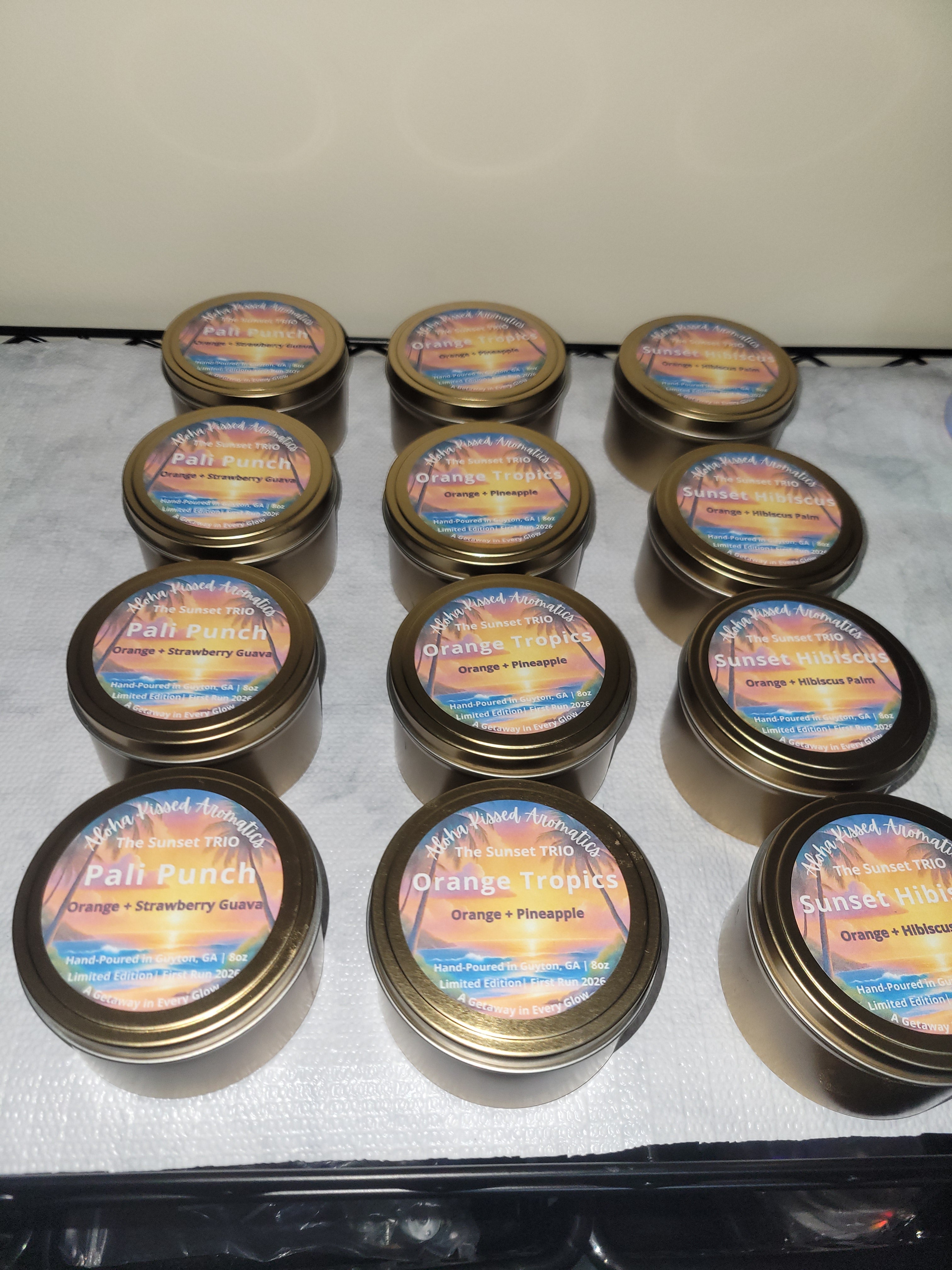 The Sunset Trio candle collection: 3 gold tins featuring Orange Tropics, Pali Punch, and Sunset Hibiscus tropical scents